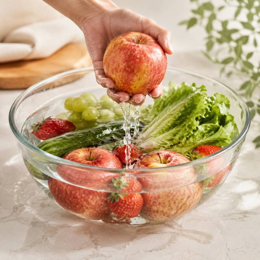 Fresh produce being lifted from a clear, complete-rinsing bowl wash